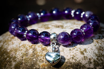 amethyst beaded bracelet with a silver heart urn charm on a stone surface